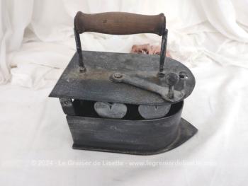 Voici un ancien fer à repasser en fonte patiné en noir avec réservoir à braises et décoré de coeurs muni d'un couvercle, de son systeme de fermeture et de son manche en bois.