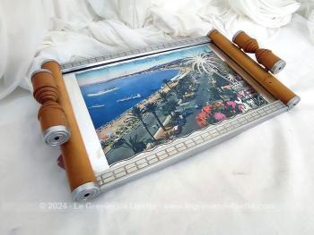 Datant des années 60, voici un plateau en bois clair serti par endroits de parties métalliques avec une vue de Nice, sa  Promenade des Anglais et l’Hôtel Négresco et recouvert d'une vitre aux décors miroir avec l'écusson de la Cote d’Azur.