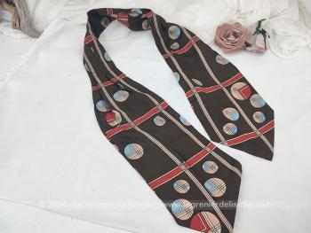 Voici un foulard forme Ascot vintage en polyester dans des coloris très tendance seventeen avec sur fond marron des cercles et raies rouges, marron et beiges, sur 122 cm de long et 15 cm de large aux extrémités.