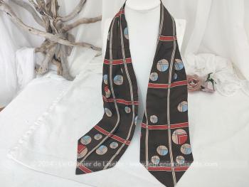 Voici un foulard forme Ascot vintage en polyester dans des coloris très tendance seventeen avec sur fond marron des cercles et raies rouges, marron et beiges, sur 122 cm de long et 15 cm de large aux extrémités.