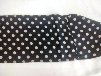 En polyester imitation soie, voici une belle lavallière noire à pois blancs décorée de petits plis religieuses avec une extrémité en biais et une droite, de 200 x 16 cm pour un joli noeud autour du cou, d'un chapeau ou autres idées.