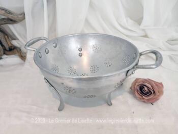 Sur 22.5 cm de diamètre, voici une ancienne passoire tripode en aluminium avec des trous pour égoutter en forme de rond et estampillée sur l'extérieur d'un pied  