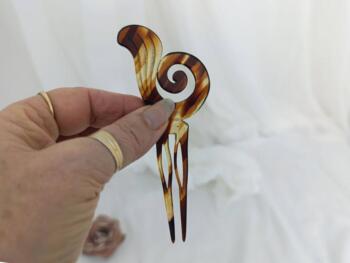 Sur 12 x 5.5 x0.2 cm, voici un superbe ancien peigne à chignon à deux dents, datant surement des années 40/50 et réalisé en rhodoïd imitation corne et portant une estampille presque illisible.