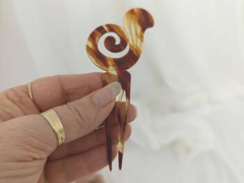 Sur 12 x 5.5 x0.2 cm, voici un superbe ancien peigne à chignon à deux dents, datant surement des années 40/50 et réalisé en rhodoïd imitation corne et portant une estampille presque illisible.