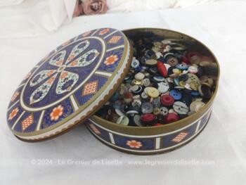 Superbe boite vintage sérigraphiée de volutes et arabesques blanches et orange sur un fond marine garnie à l'intérieur de 300 g de boutons.