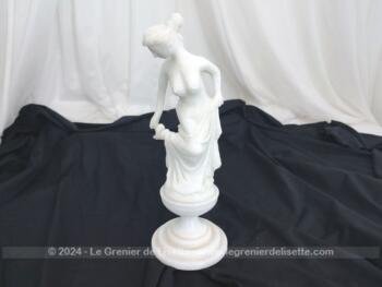 Voici une belle statuette, sculpture en albâtre blanc d'une jeune femme dévêtue, son vêtement glissant le long de ses jambes et tenant sa chaussure.  Superbe !