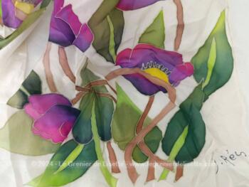 Sur 40 x 140 cm, voici une belle écharpe en soie naturelle ivoire avec aux deux extrémités de larges décors de fleurs peintes à la main dans des tons de mauve, jaune et verts et portant une signature.