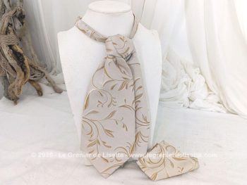 Voici une belle cravate Ascot à l'allure vintage en tissus 100% polyester beige aux dessins de volutes couleur caramel surlignées d'un liseré brillant avec une pochette assortie.