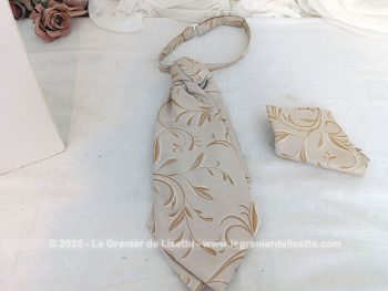 Voici une belle cravate Ascot à l'allure vintage en tissus 100% polyester beige aux dessins de volutes couleur caramel surlignées d'un liseré brillant avec une pochette assortie.