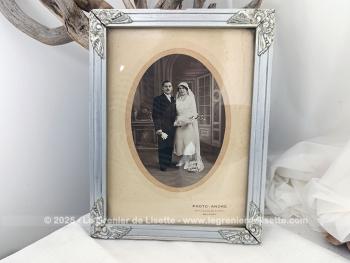 Sur 27 x 21 x 1cm, voici un cadre en bois peint couleur vieil argent  avec des fleurs en reliefs aux angles et  mettant en valeur une photo d'un mariage du début du siècle.  Tout dans ce cadre nous transporte avec nostalgie dans le monde vintage des années 30!
