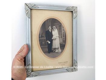 Sur 27 x 21 x 1cm, voici un cadre en bois peint couleur vieil argent  avec des fleurs en reliefs aux angles et  mettant en valeur une photo d'un mariage du début du siècle.  Tout dans ce cadre nous transporte avec nostalgie dans le monde vintage des années 30!