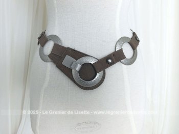 Sur 94 cm de long et 7 cm de large, voici une ceinture vintage, totalement dans le look des années 70 et composée de morceaux d'élastique marron reliant entre eux 7 larges anneaux en métal martelé, dont le dernier sert de fermeture.