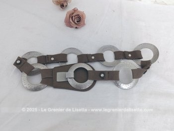 Sur 94 cm de long et 7 cm de large, voici une ceinture vintage, totalement dans le look des années 70 et composée de morceaux d'élastique marron reliant entre eux 7 larges anneaux en métal martelé, dont le dernier sert de fermeture.