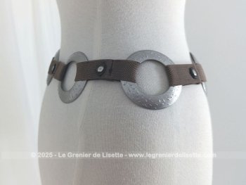 Sur 94 cm de long et 7 cm de large, voici une ceinture vintage, totalement dans le look des années 70 et composée de morceaux d'élastique marron reliant entre eux 7 larges anneaux en métal martelé, dont le dernier sert de fermeture.