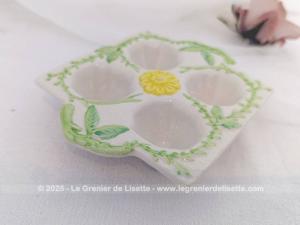 Voici un présentoir vintage pour 4 oeufs en céramique couleur ivoire et décoré de feuillage vert et d'une fleur jaune au centre. Au dos, une estampille, un tampon complétement illisible.