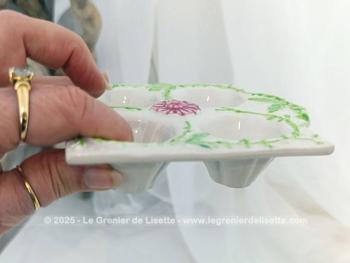 Voici un présentoir vintage pour 4 oeufs en céramique couleur ivoire et décoré de feuillage vert et d'une fleur fuchsia au centre. Au dos, une estampille, un tampon complétement illisible.