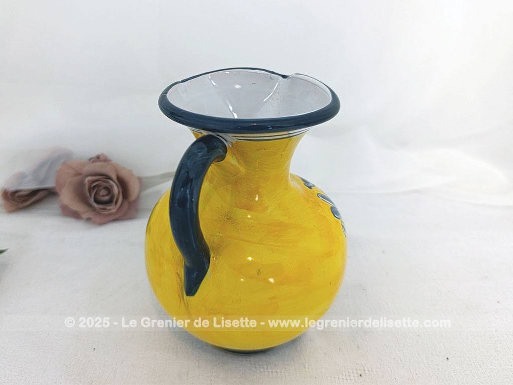 Voici un beau pichet vintage, surement originaire d'Espagne, signé et numéroté, avec sur un fond jaune foncé des décors d'un personnage peint en gris bleu avec des fleurs.