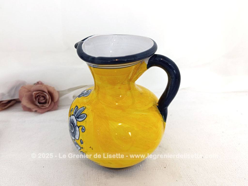 Voici un beau pichet vintage, surement originaire d'Espagne, signé et numéroté, avec sur un fond jaune foncé des décors d'un personnage peint en gris bleu avec des fleurs.