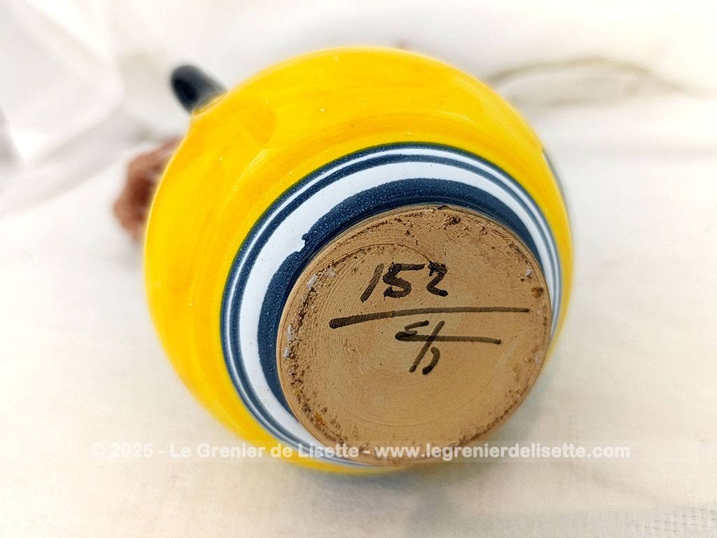 Voici un beau pichet vintage, surement originaire d'Espagne, signé et numéroté, avec sur un fond jaune foncé des décors d'un personnage peint en gris bleu avec des fleurs.