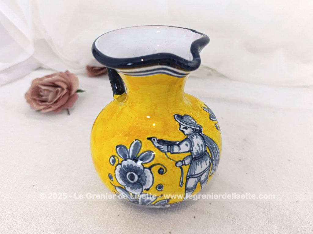 Voici un beau pichet vintage, surement originaire d'Espagne, signé et numéroté, avec sur un fond jaune foncé des décors d'un personnage peint en gris bleu avec des fleurs.
