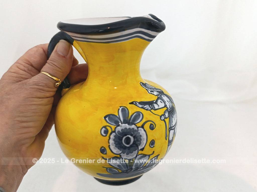 Voici un beau pichet vintage, surement originaire d'Espagne, signé et numéroté, avec sur un fond jaune foncé des décors d'un personnage peint en gris bleu avec des fleurs.