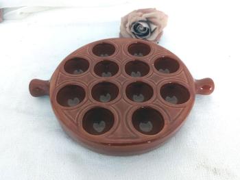 En céramique émaillée brun, voici un plat de présentation avec 12 emplacements et deux poignées, estampillé Emile Henry France  25 - 12. Idéal pour escargots, oeufs  ou autres idées culinaires de décoration.