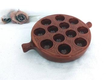 En céramique émaillée brun, voici un plat de présentation avec 12 emplacements et deux poignées, estampillé Emile Henry France  25 - 12. Idéal pour escargots, oeufs  ou autres idées culinaires de décoration.
