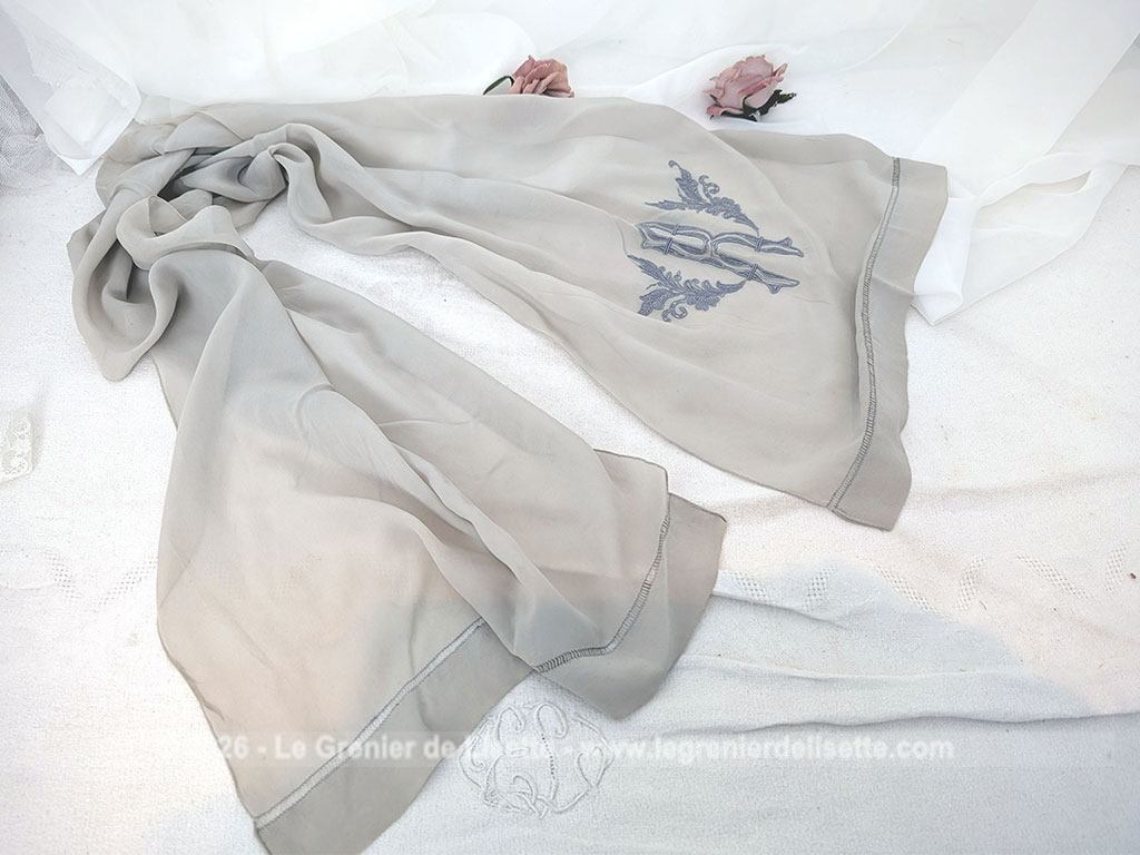 Fait main, voici une écharpe en voile de crêpe gris taupe de 80 x 154 cm, orné d'un grand R brodé et décoré aux extrémités d'un jour de Venise. Pour une écharpe discrète, originale et unique.