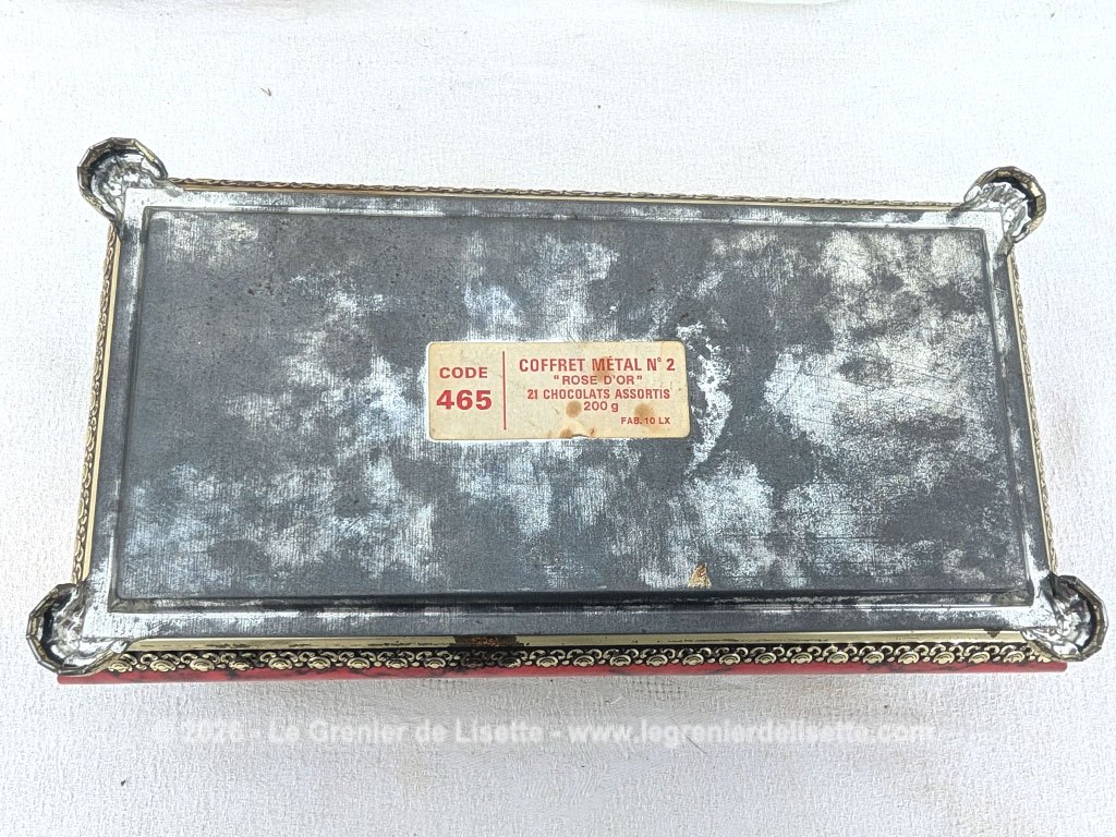 De forme rectangulaire, voici une ancienne belle boite métallique sérigraphiée en rouge, noir et or avec sur le couvercle une fleur dorée en relief et ses 4 pieds ouvragés