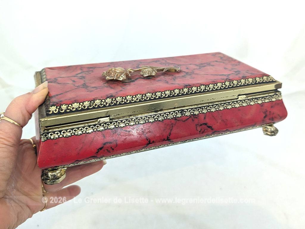 De forme rectangulaire, voici une ancienne belle boite métallique sérigraphiée en rouge, noir et or avec sur le couvercle une fleur dorée en relief et ses 4 pieds ouvragés