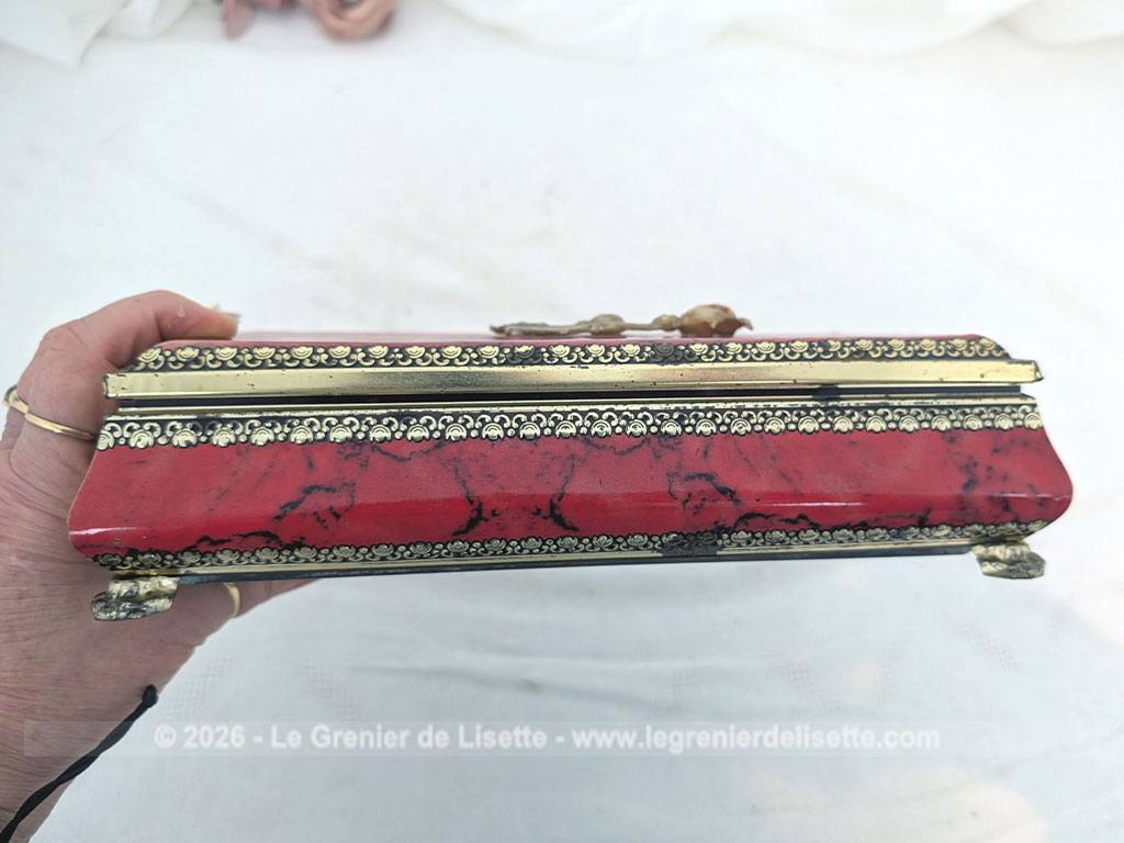 De forme rectangulaire, voici une ancienne belle boite métallique sérigraphiée en rouge, noir et or avec sur le couvercle une fleur dorée en relief et ses 4 pieds ouvragés