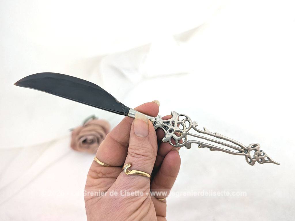 Voici un élégant coupe-papier des années 90, composé d'une lame en plastique épais noir, peut-être en bakélite à la ligne courbe et d'un manche en métal argenté aux motifs ciselés très décoratifs. Pièce artisanale pleine de charme qui remplit parfaitement sa fonction avec originalité.