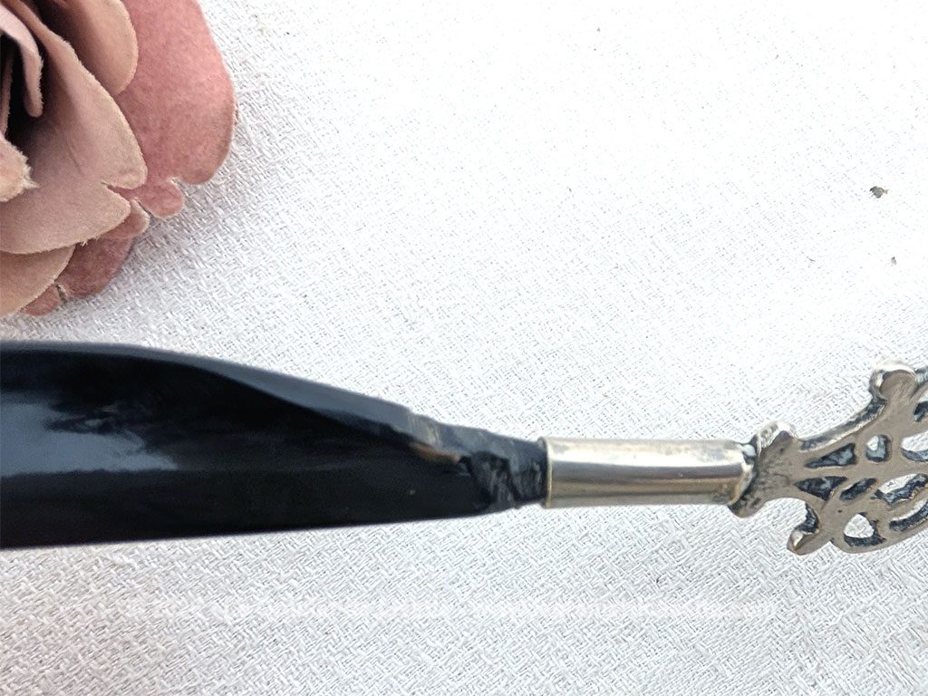 Voici un élégant coupe-papier des années 90, composé d'une lame en plastique épais noir, peut-être en bakélite à la ligne courbe et d'un manche en métal argenté aux motifs ciselés très décoratifs. Pièce artisanale pleine de charme qui remplit parfaitement sa fonction avec originalité.