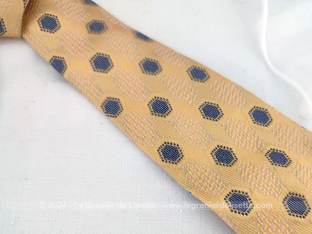 Elégante cravate vintage de la prestigieuse maison Pierre Cardin, 100% soie ocre jaune rehaussée de motifs géométriques tissés bleu et blanc, un style rétro chic très raffiné.