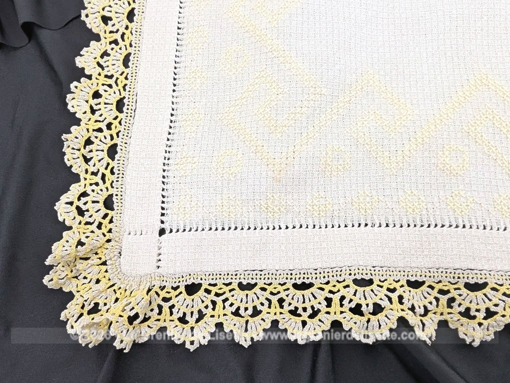 Ancien napperon original brodé de motifs géométriques au point de croix en fil jaune et bordé de dentelle aux fuseaux bicolore. Fait main et pièce unique.