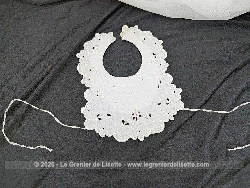 Voici un délicat bavoir ancien en délicat coton blanche, orné d'un beau travail de broderie anglaise aux motifs floraux avec des bordures festonnées. Deux liens d'origine pour l'attache au dos et un bouton au cou. Du beau linge ancien de qualité.