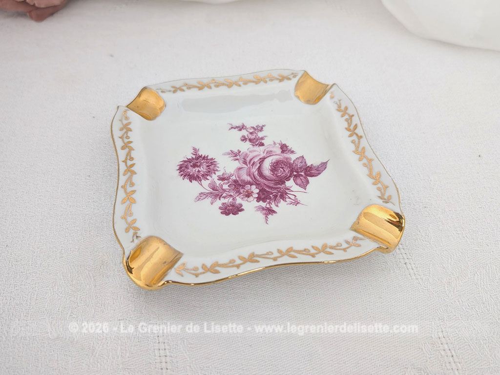 Sur 12 x 12 x 2 cm, voici un petit cendrier vintage en porcelaine de Limoges au décor floral rose fuchsia au centre. La pièce est soulignée par une frise de feuilles dorées sur le pourtour et 4 encoches généreusement rehaussées d'or. Le tampon