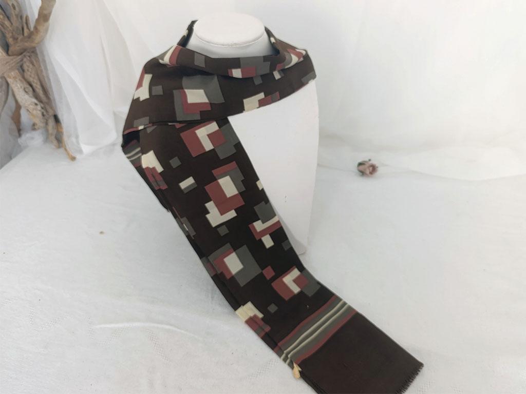 Sur 24 x 138 cm, voici un foulard vintage pour homme, en polyester, sur fond couleur chocolat on découvre des dessins de formes géométriques couleurs caramel, taupe et écru, vraiment tendance seventies. A porter façon