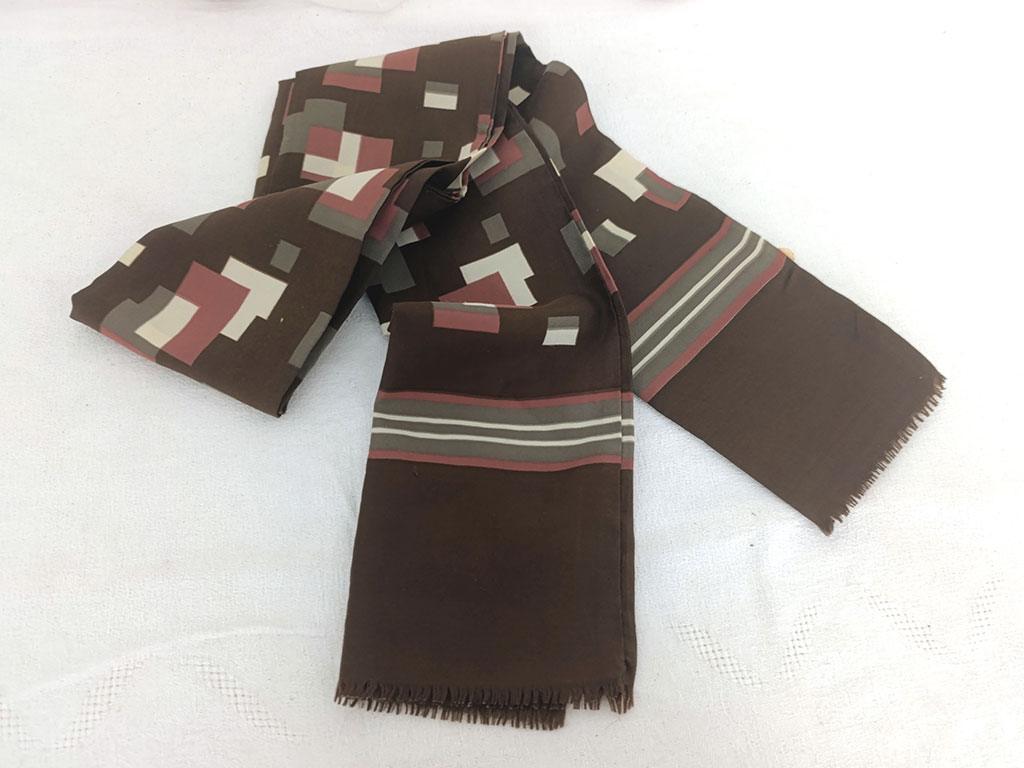Sur 24 x 138 cm, voici un foulard vintage pour homme, en polyester, sur fond couleur chocolat on découvre des dessins de formes géométriques couleurs caramel, taupe et écru, vraiment tendance seventies. A porter façon