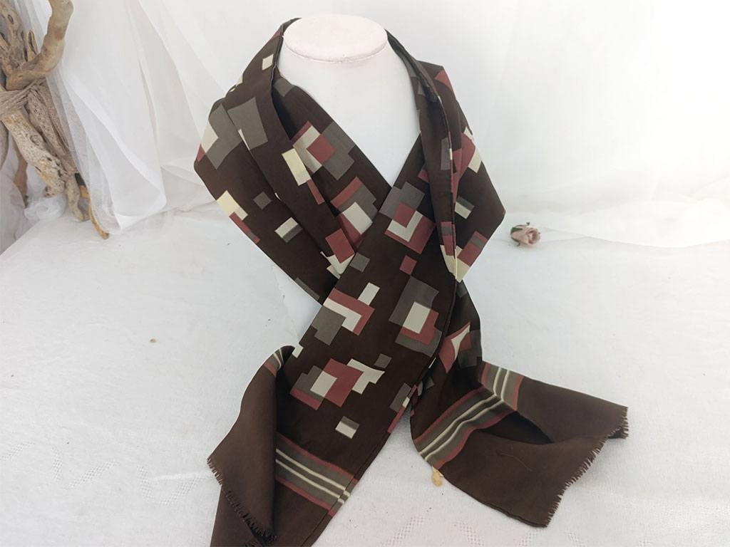 Sur 24 x 138 cm, voici un foulard vintage pour homme, en polyester, sur fond couleur chocolat on découvre des dessins de formes géométriques couleurs caramel, taupe et écru, vraiment tendance seventies. A porter façon
