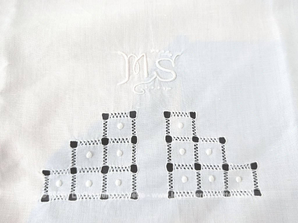 Voici un magnifique drap ancien de 90 x 126 cm pour berceau ou lit de bébé en coton blanc orné d'un superbe travail de jours de broderies géométriques et d'un élégant monogramme MS brodé à la main.