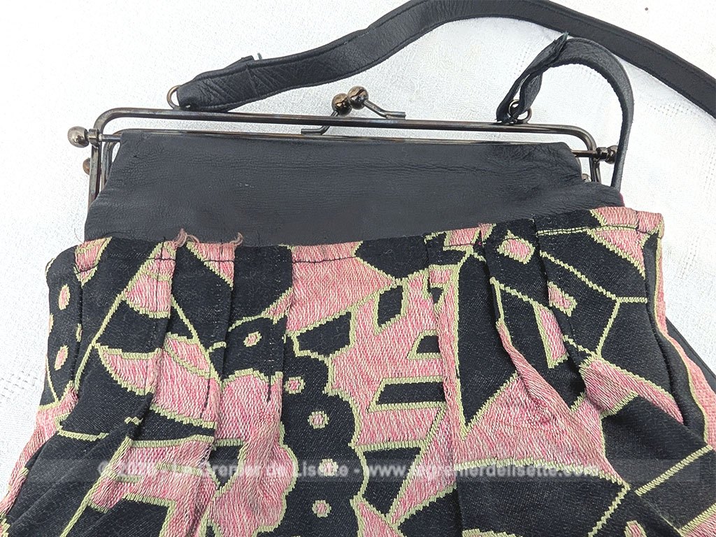 De la marque "Emma Blonde", voici un superbe sac minaudière vintage en tissu jacquard noir et rose très Art Déco, avec un haut en cuir noir et fermé par une armature en métal et doublé d'un satin fuchsia. A porterà l'épaule grâce à sa bandoulière en cuir noir ou à la main. Années 2000.