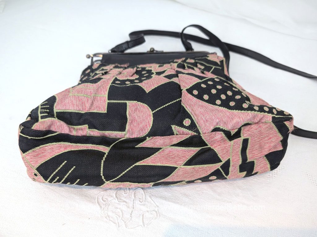 De la marque "Emma Blonde", voici un superbe sac minaudière vintage en tissu jacquard noir et rose très Art Déco, avec un haut en cuir noir et fermé par une armature en métal et doublé d'un satin fuchsia. A porterà l'épaule grâce à sa bandoulière en cuir noir ou à la main. Années 2000.