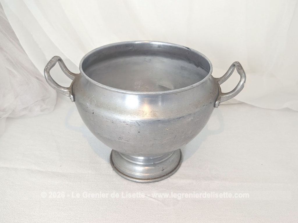 Voici un corps de soupière vintage en aluminium au charme rustique et authentique avec sa ligne ventrue qui repose sur un élégant piédouche et ses deux anses rivetées. Proposée sans son couvercle elle se transforme idéalement en un grand saladier, cache pot ou un centre de table de caractère.