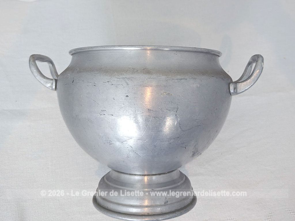 Voici un corps de soupière vintage en aluminium au charme rustique et authentique avec sa ligne ventrue qui repose sur un élégant piédouche et ses deux anses rivetées. Proposée sans son couvercle elle se transforme idéalement en un grand saladier, cache pot ou un centre de table de caractère.