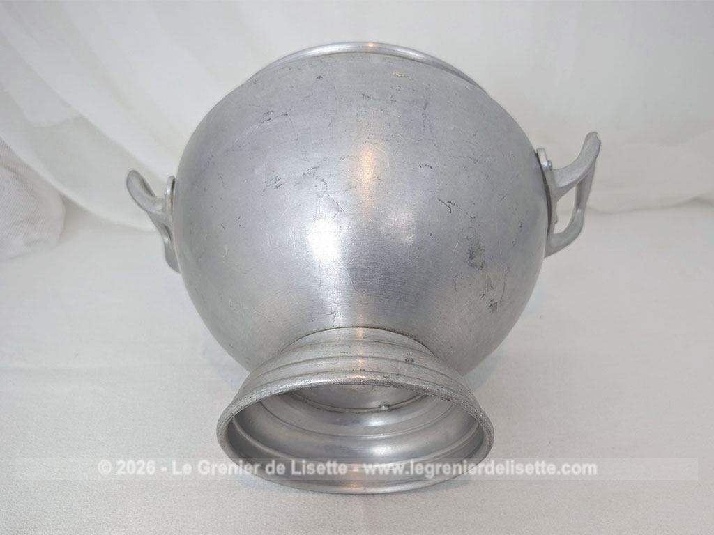 Voici un corps de soupière vintage en aluminium au charme rustique et authentique avec sa ligne ventrue qui repose sur un élégant piédouche et ses deux anses rivetées. Proposée sans son couvercle elle se transforme idéalement en un grand saladier, cache pot ou un centre de table de caractère.